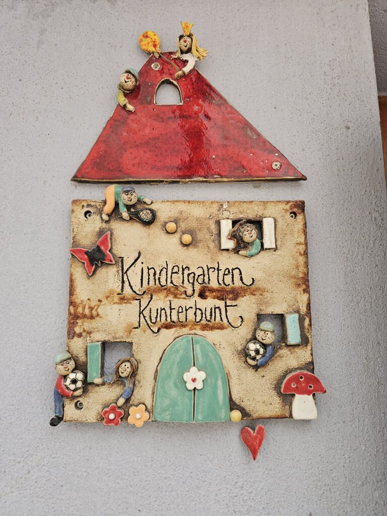 Türschild aus Ton, in Form eines Hauses, Kinder schauen aus dem Fester und spielen mit Kindern vor dem Haus